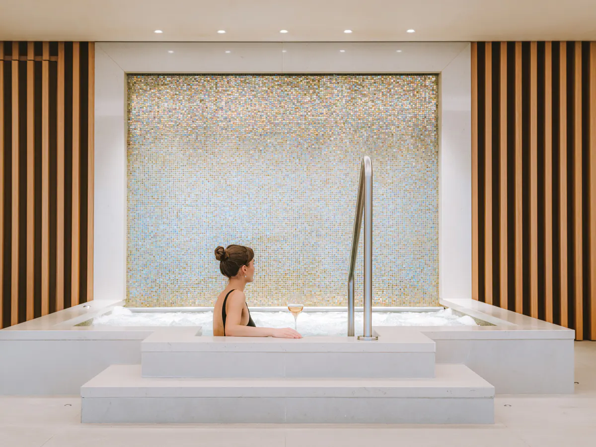 Woman in spa tub with marble mosaic backdrop and vertical wood slat detailing