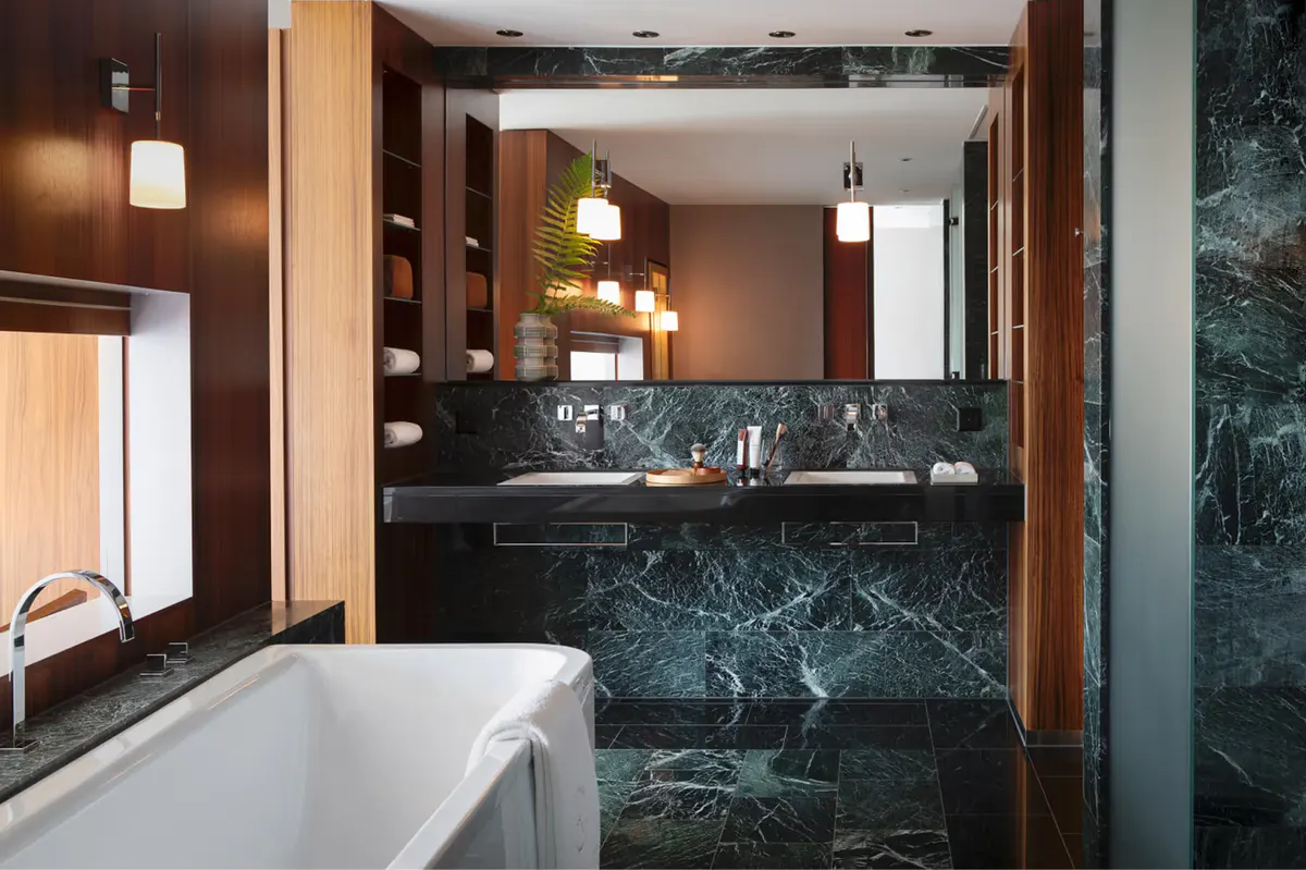 Luxury bathroom with dark marble, freestanding tub, wood accents, and illuminated mirror
