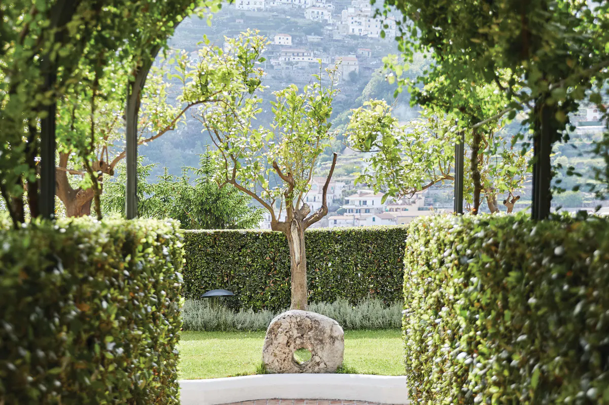 Garden corridor framed by trimmed hedges with lawn and scenic coastal vista beyond