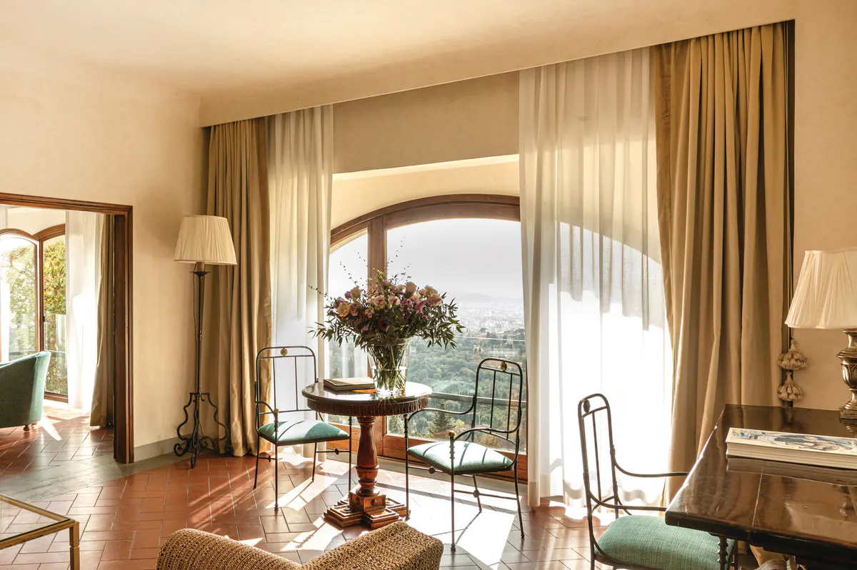 A sitting room with full-length doors, garden views, round table with flowers, and warm wood tones