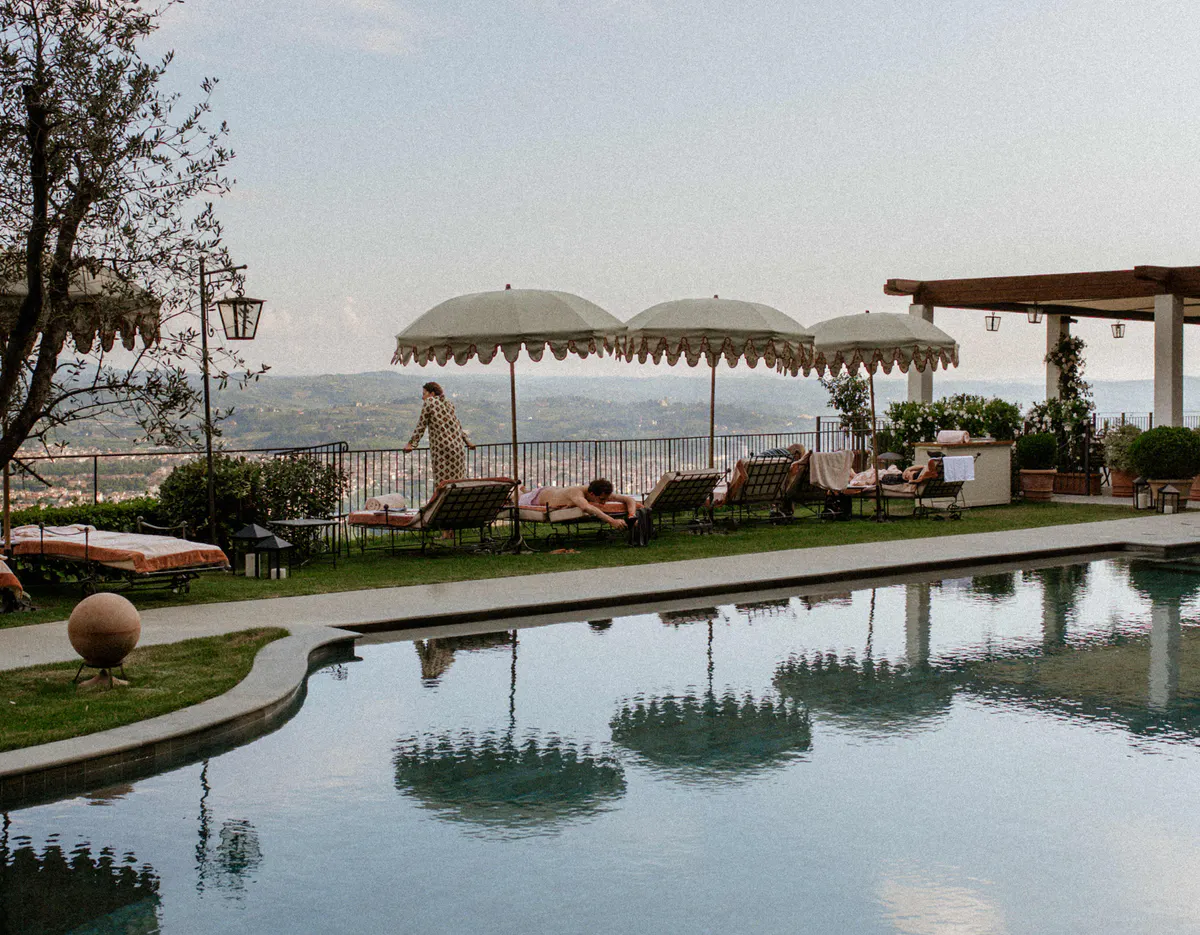 A swimming pool with cypress alleys, terrace seating, and Tuscan valley views beyond