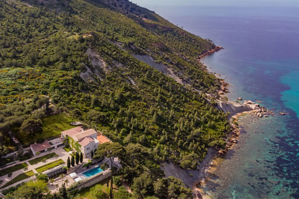 Aerial view of clifftop estate with Mediterranean forest, turquoise waters, and sailboat