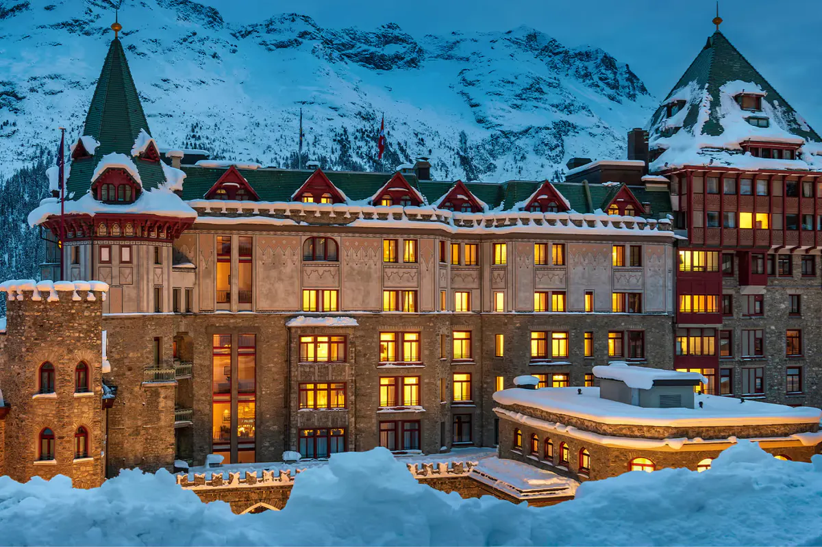 Illuminated hotel facade in evening snow with dark mountains behind