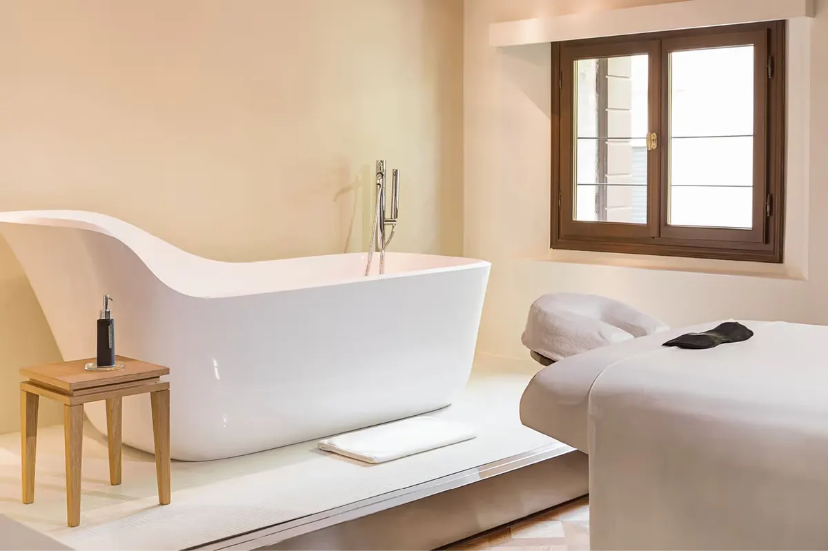 A spa bathroom with a freestanding white stone tub, stepped platform, and window with natural light