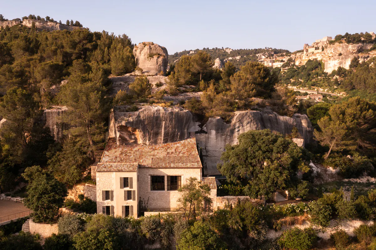 Aerial view of terra-cotta-roofed villa complex carved among limestone formations, cypress, forested valley