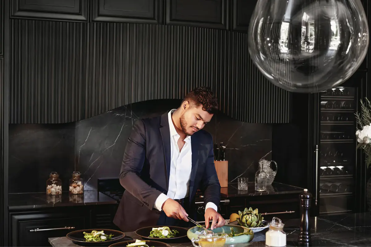 Chef in dark jacket preparing food at white countertop under pendant lighting