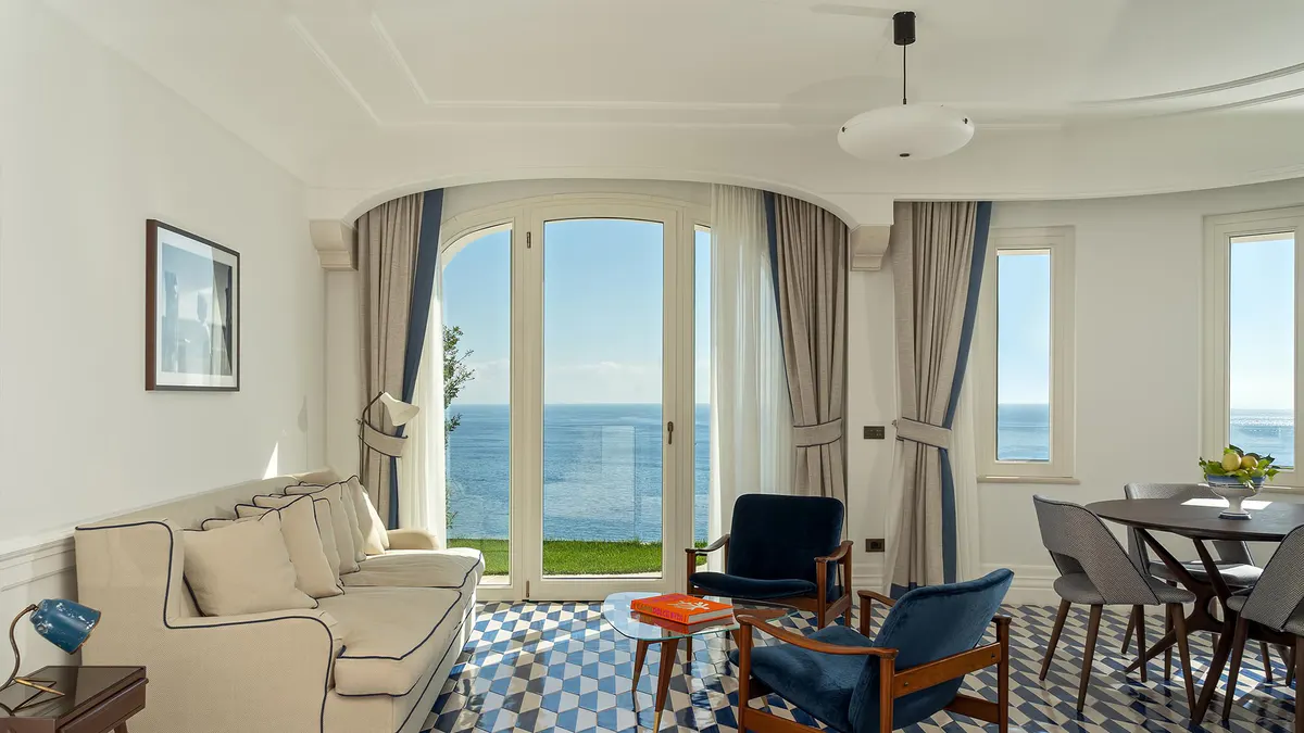 Light-filled room with patterned flooring, arched windows framing sea vista, and seating area