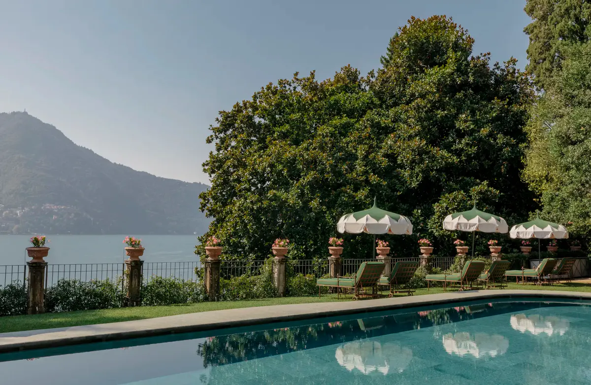 A rectangular pool reflecting cypress trees with Lake Como and mountains in the distance