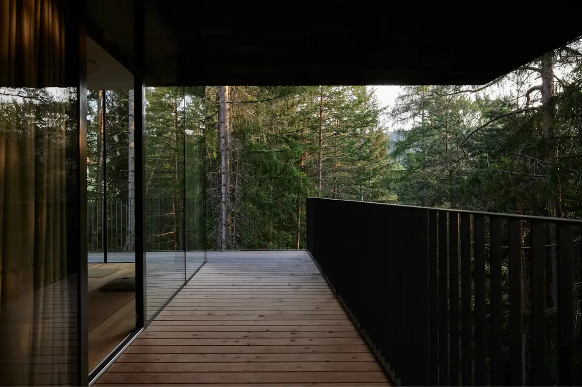 Wooden deck with glass railing overlooking forested mountainous terrain