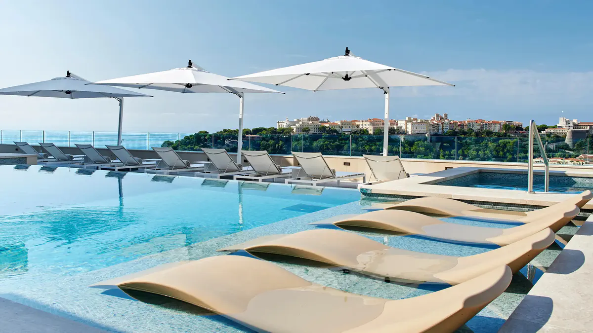 Rooftop pool with blue water, white umbrellas, and lounge chairs overlooking water