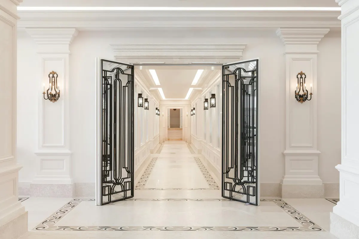 Interior hallway with white stone walls, ornate brass sconces, and decorative iron double doors