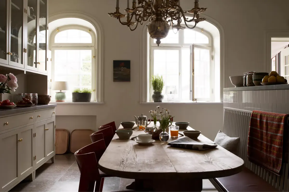 A dining room with round marble table, arched windows, white chairs, and pendant lighting
