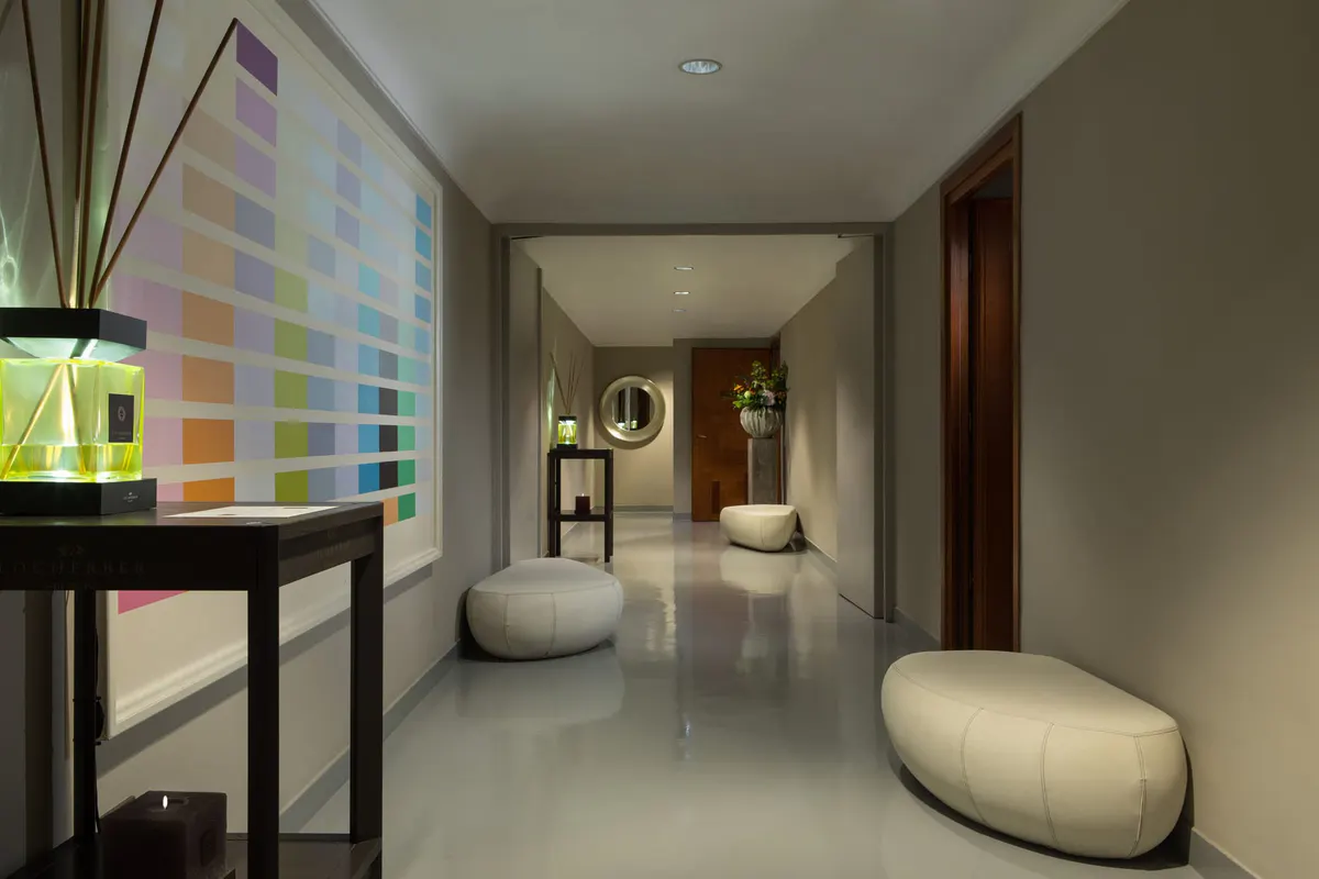 Modern spa corridor with soft lighting, rounded poufs, and color palette samples on wall