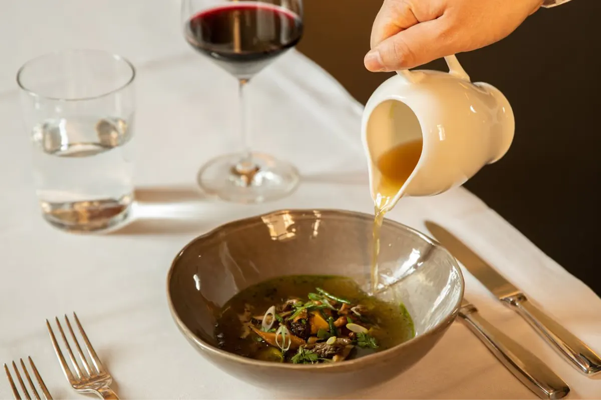 A plated dish of pasta with sauce and garnish being served at a table with wine and glassware