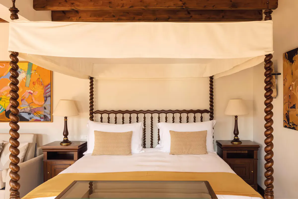 Canopied four-poster bed with cream linens in a suite with wooden furnishings
