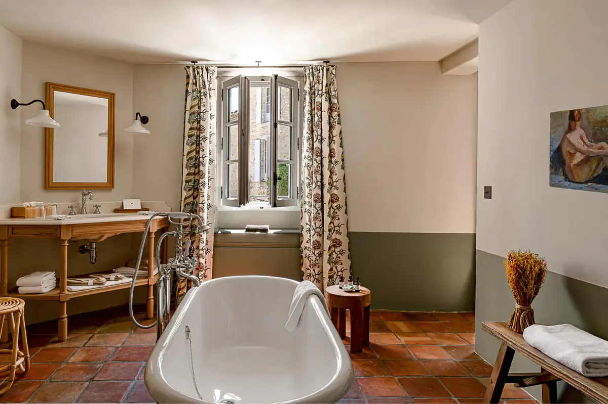 A white freestanding bathtub in a stone bathroom with half-painted green walls and wooden furniture