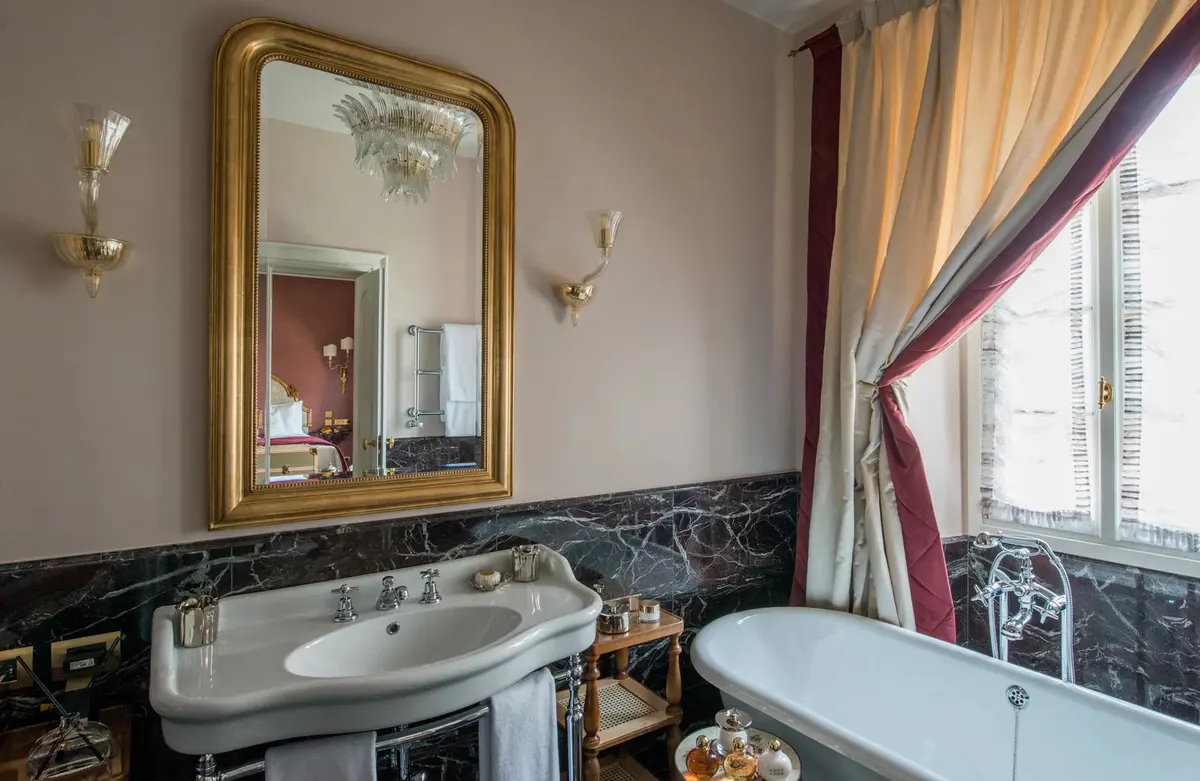 A bathroom with gold-framed mirror, pedestal sink, and slate accent wainscoting