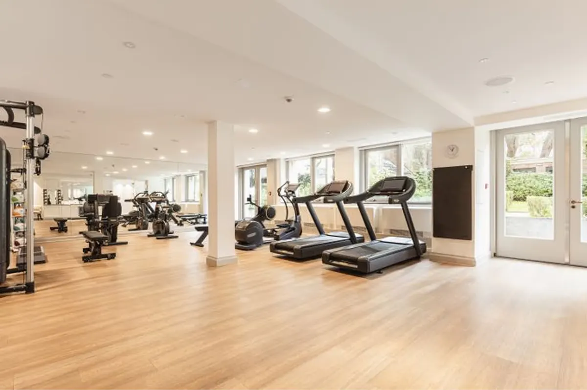 A fitness center with treadmills and exercise equipment on light wood flooring with bright natural light