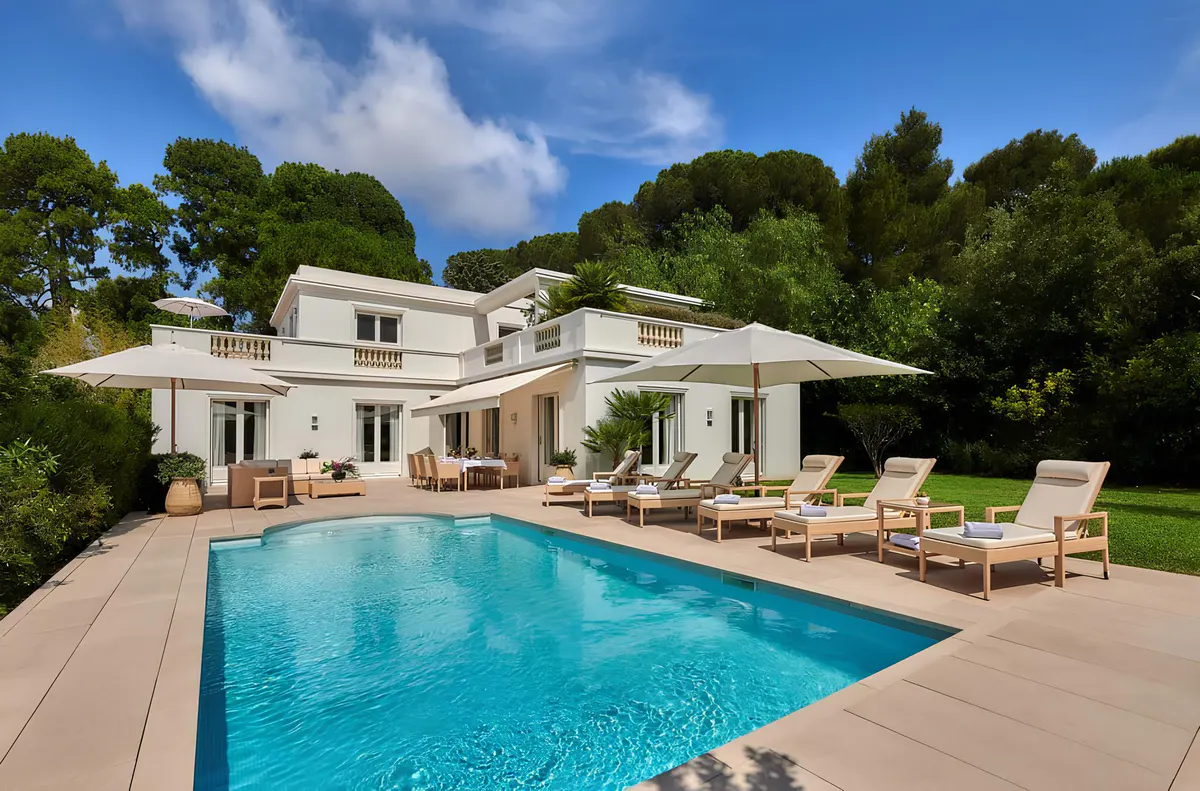 An aerial view of a pink Mediterranean villa with a turquoise pool and surrounding manicured grounds
