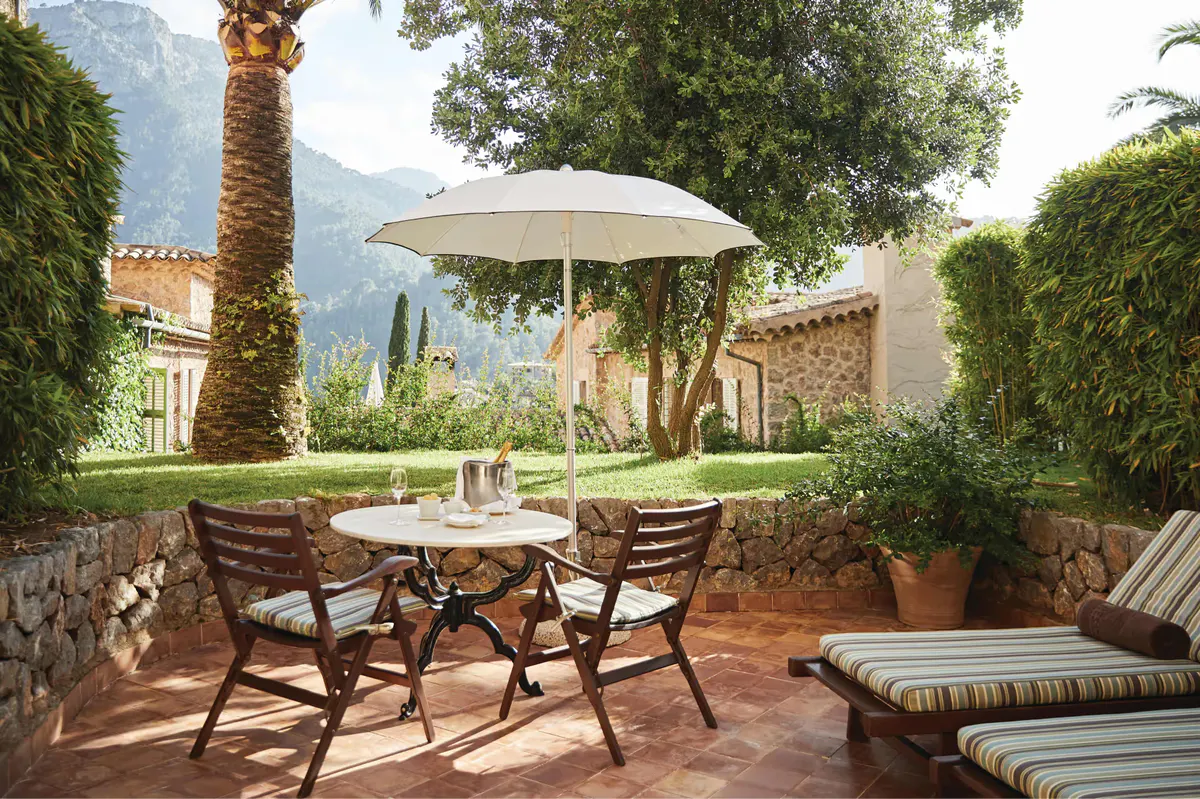 Shaded courtyard with dining table, chairs, and turquoise pool surrounded by cypress trees