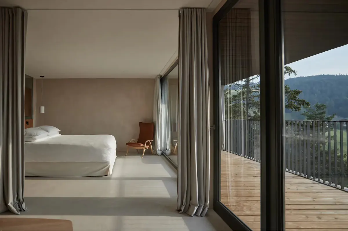 Bright bedroom with white bedding, wood accents, and open doors to a terrace with mountain views