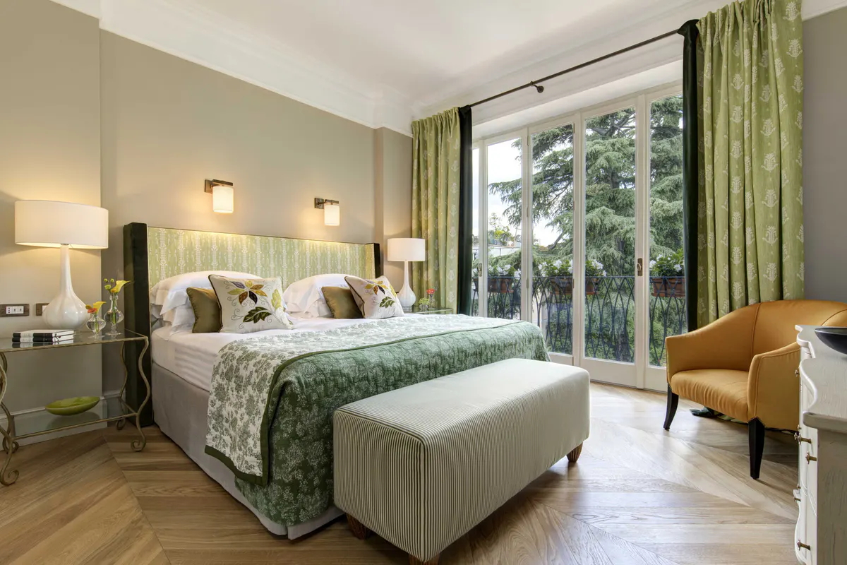 Bedroom with green patterned bedspread, marble accents, and large windows with garden views