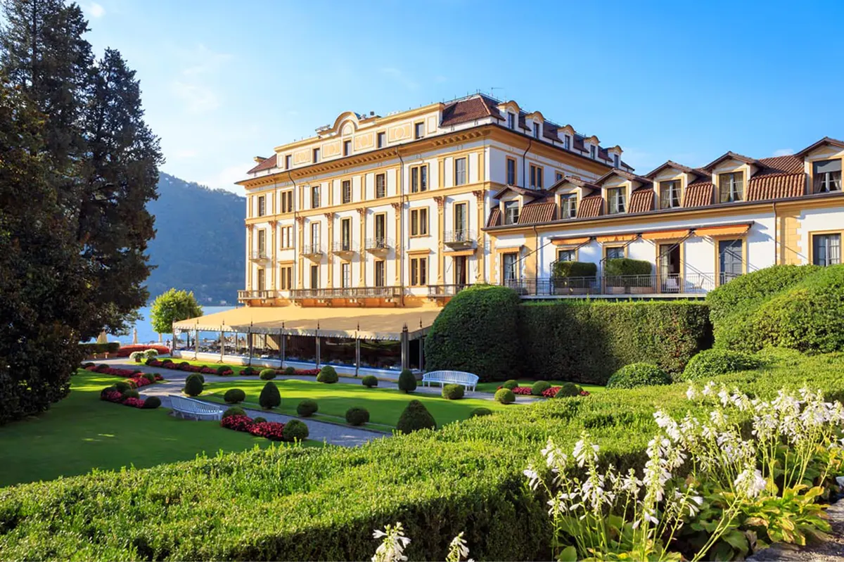 Pale yellow Renaissance palazzo with sloped roof overlooking manicured gardens and lake