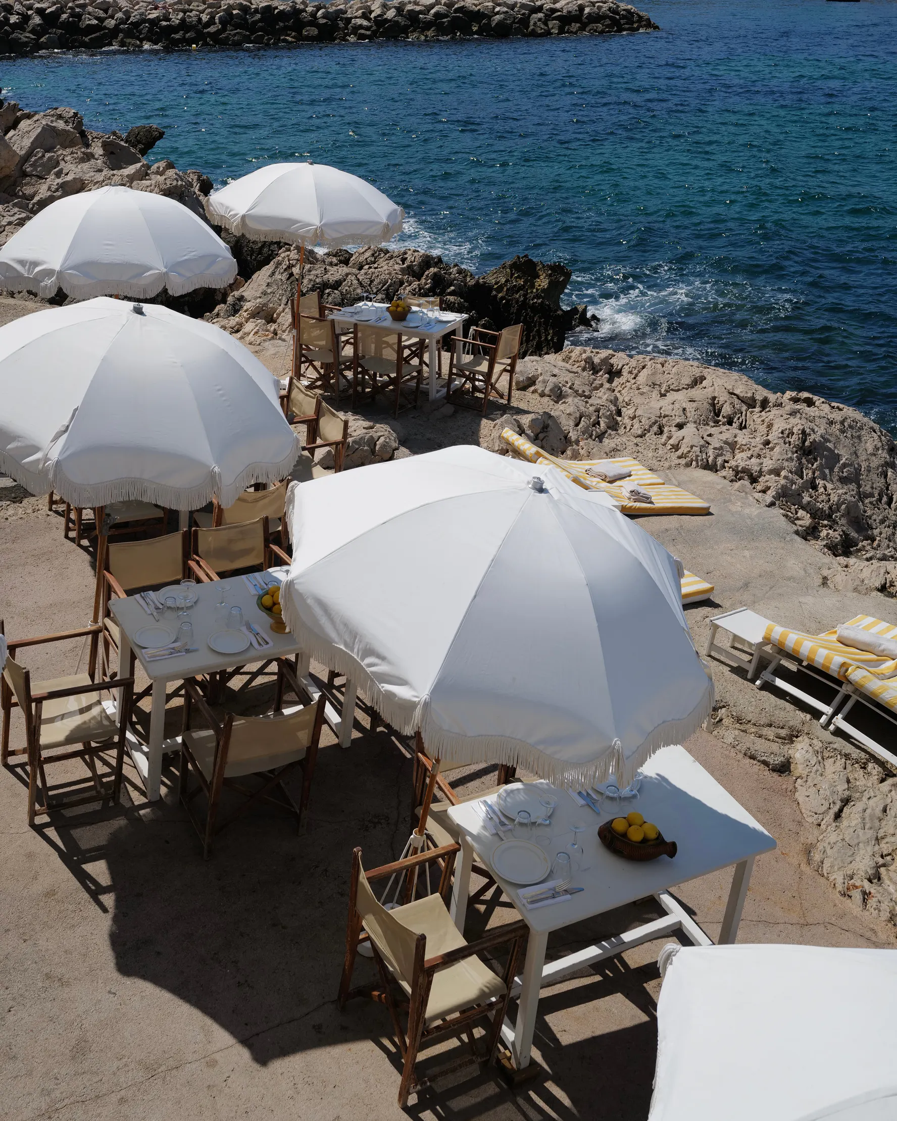 White parasols and canvas chairs set out on the rocks at Tuba Club, the sea beyond