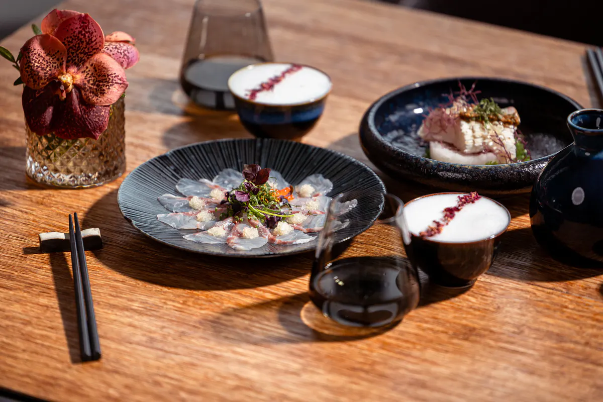 Plated cuisine on dark ceramic dishes with wine and floral arrangement
