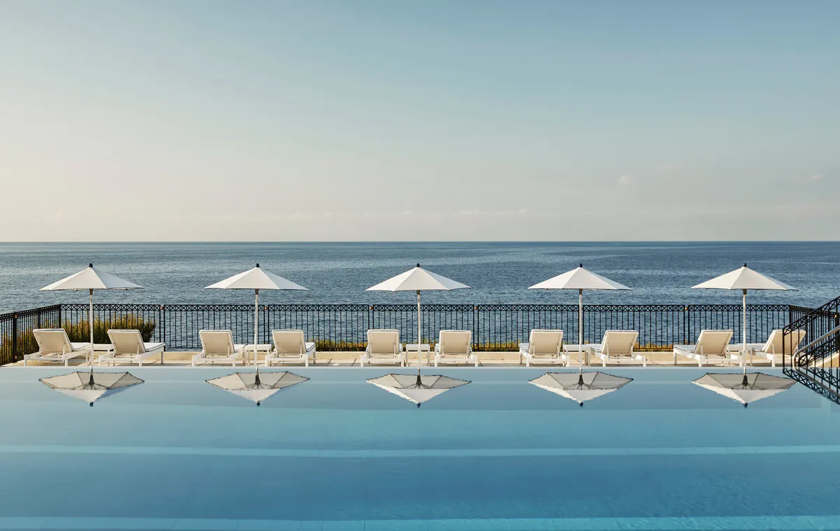 Outdoor pool with beach cabanas lined along calm Mediterranean waters