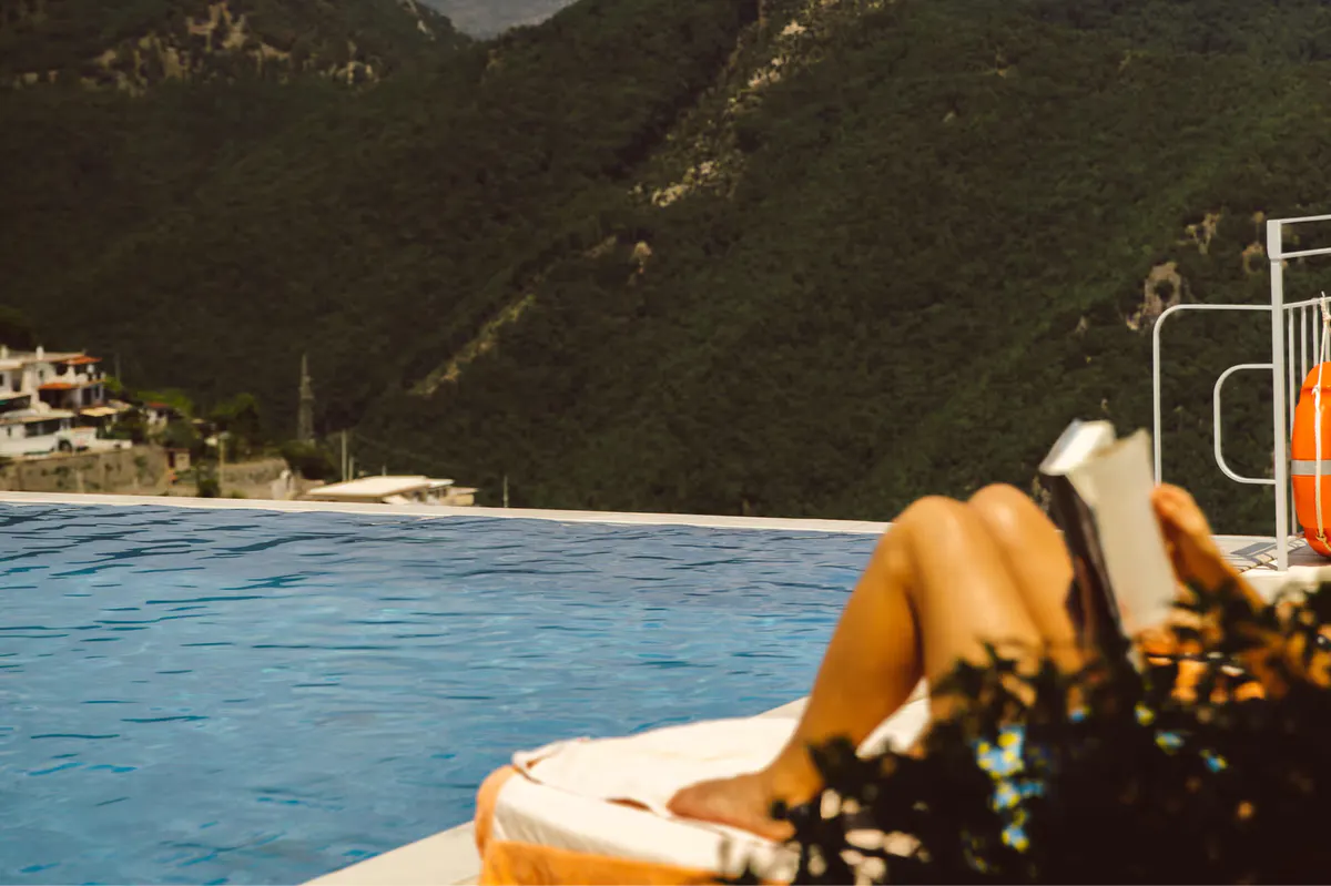 Blue infinity pool edge with yellow lounger overlooking rocky coastline and terraced village below