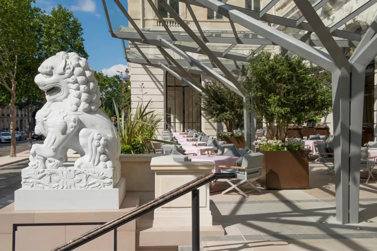Dining terrace under pergola with pink flowers, green vines, and dressed tables in daylight