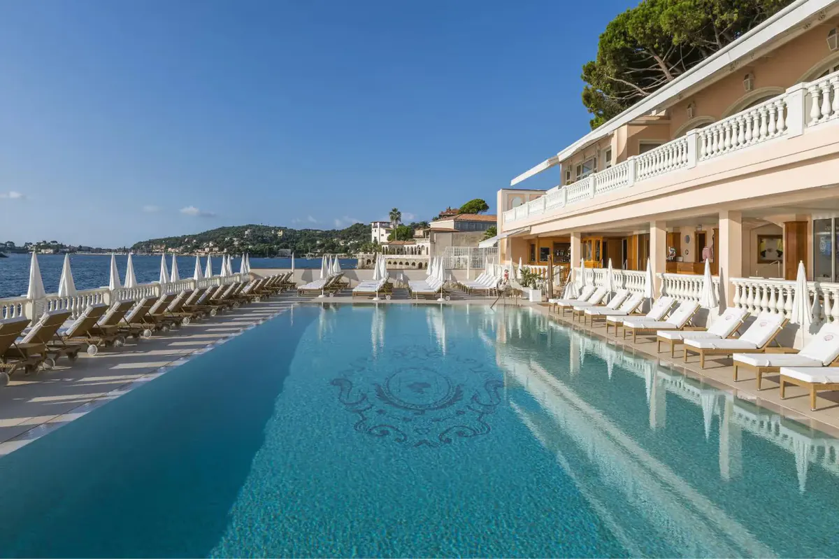 Long pool with deck loungers and Mediterranean shoreline in the distance