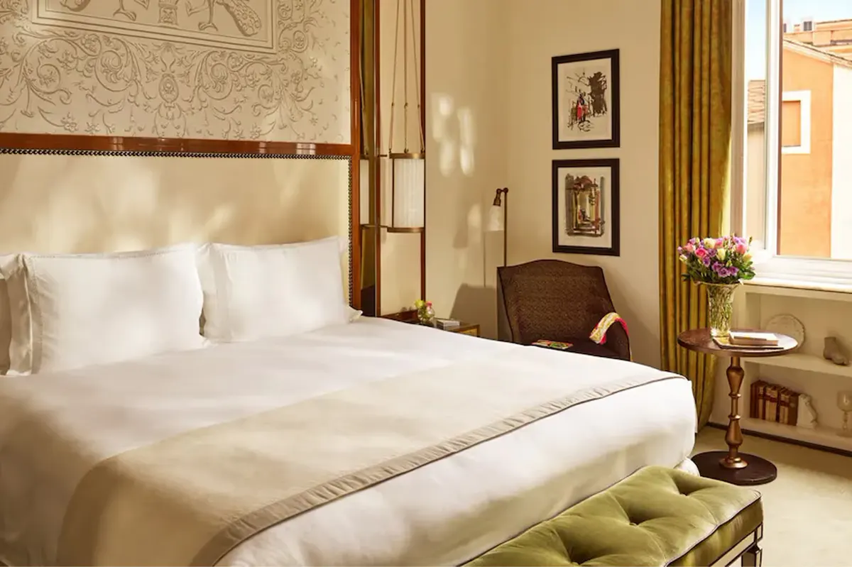 A bedroom with a canopy bed, taupe headboard, window with gold curtains, and dark wood nightstands