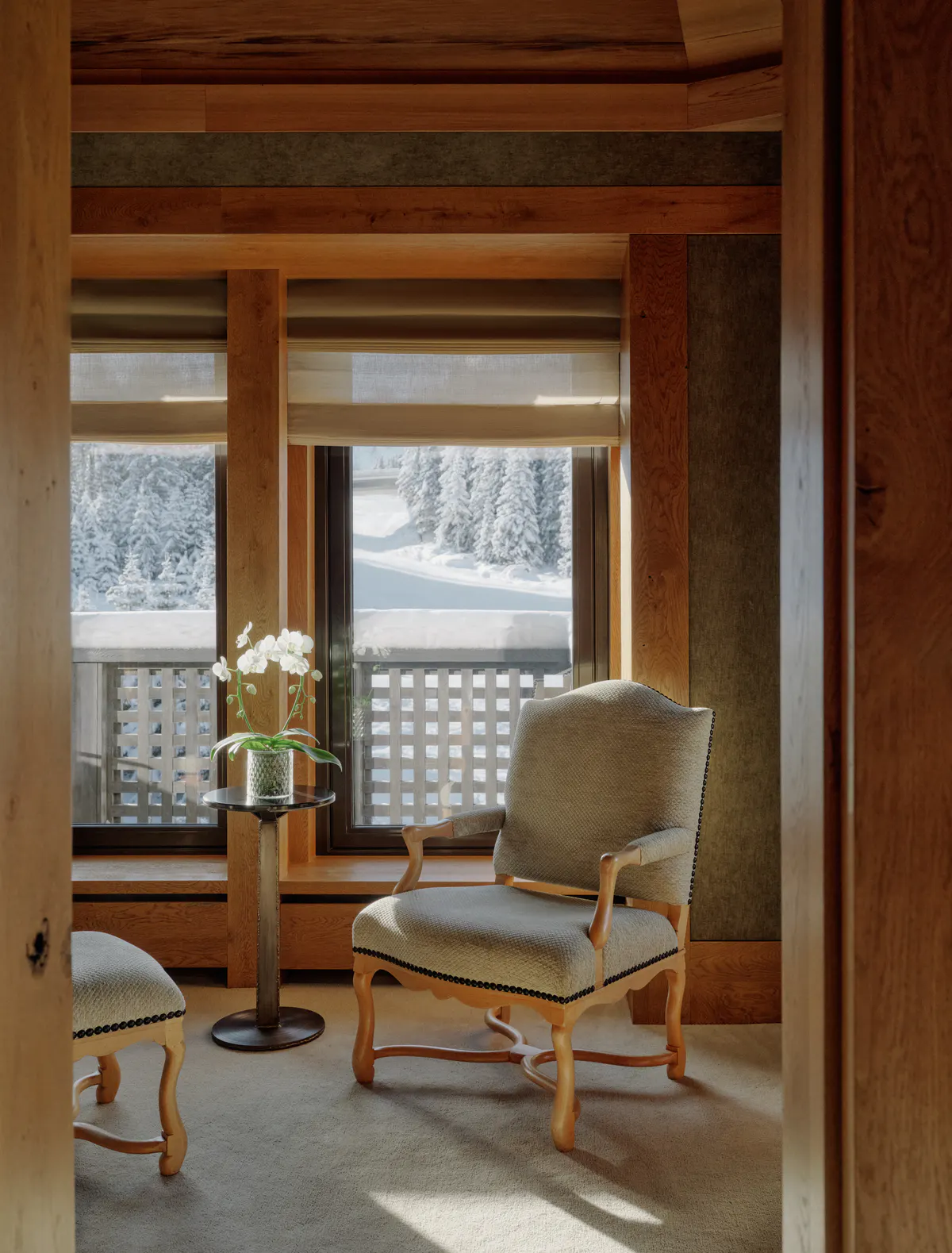 Reading nook with an upholstered armchair, ottoman, and orchid table beside a snowy window