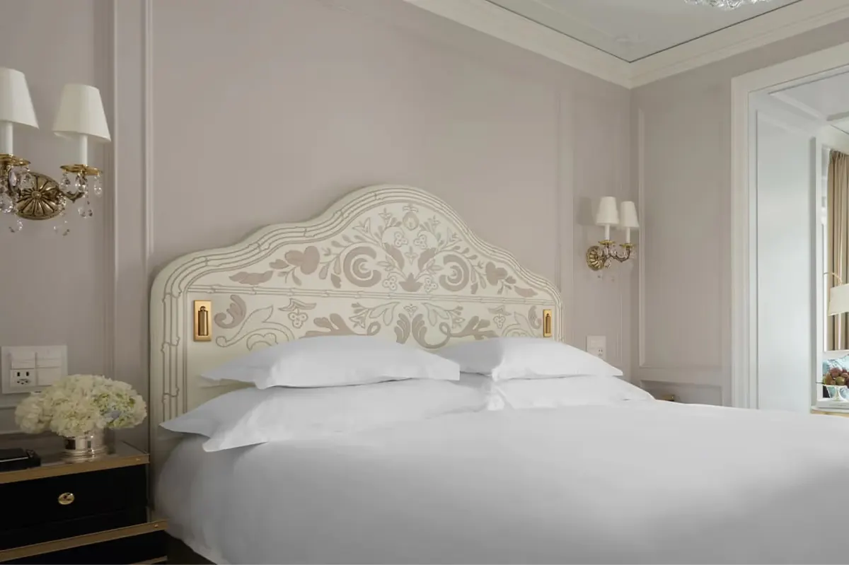 Bedroom with ornate headboard, white bedding, and classic wall sconces