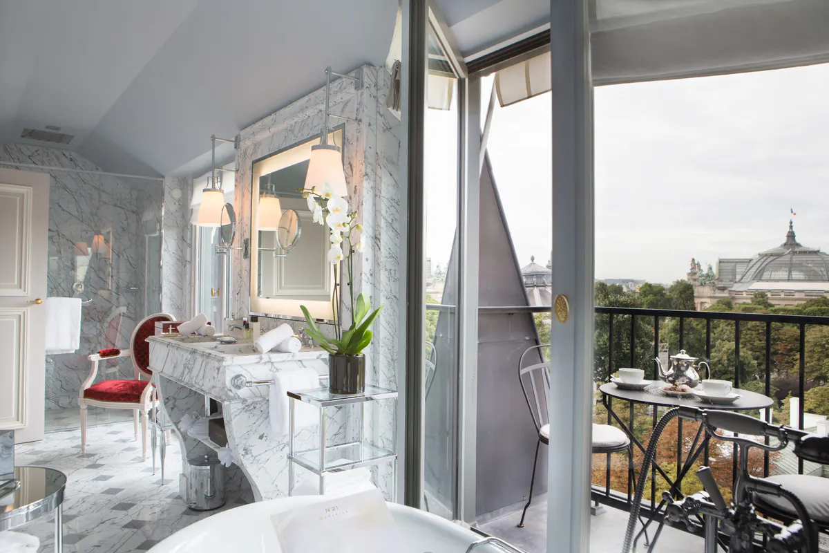 A bathroom with white marble, a red accent wall, and a mirrored vanity with Paris rooftop views