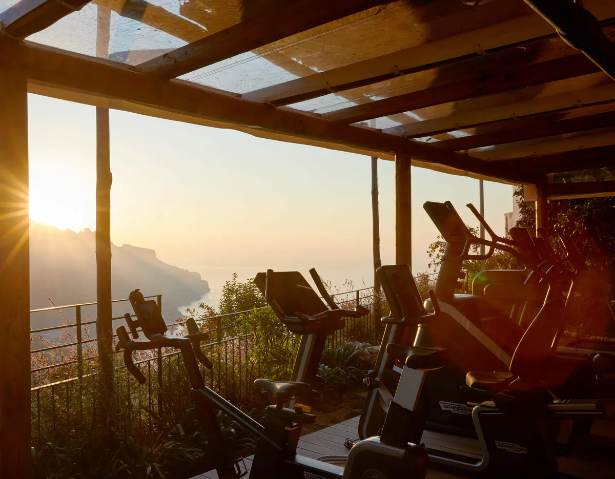 Fitness room overlooking coast at sunset with exercise equipment and mountain silhouettes