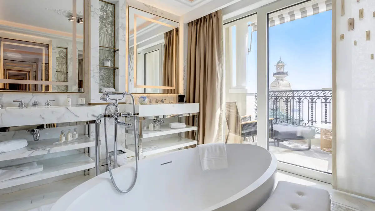 Bathroom in white marble with soaking tub and balcony door overlooking the sea