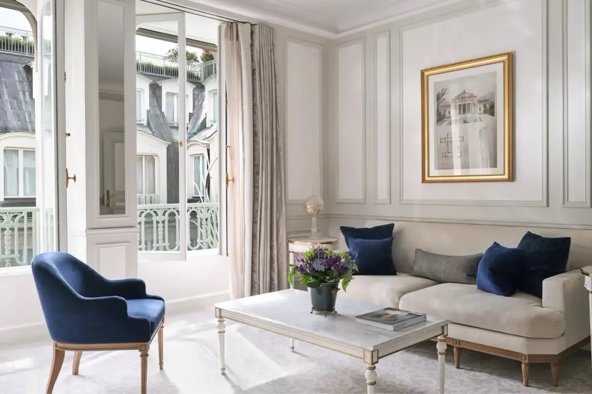 A sitting area with velvet sofa and classical furnishings beside windows with floor-to-ceiling drapes