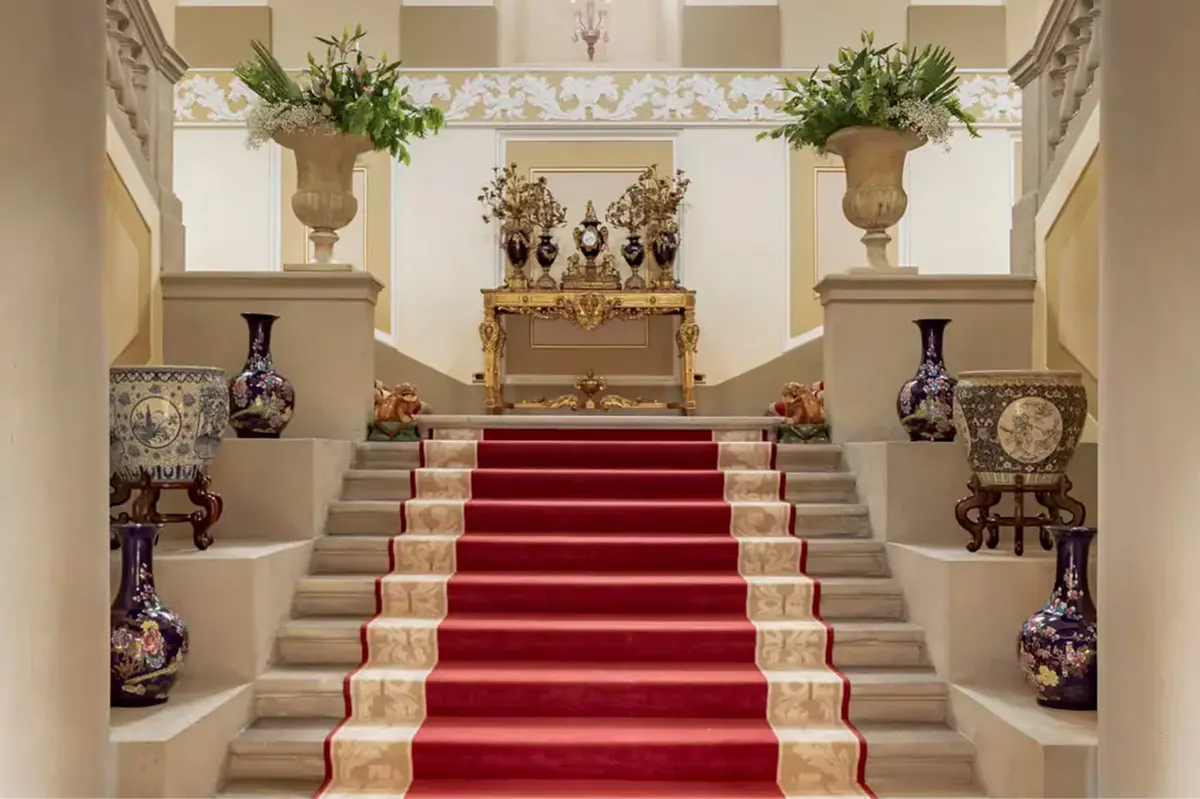 A grand staircase with marble treads, green carpet runner, and ornate balustrades