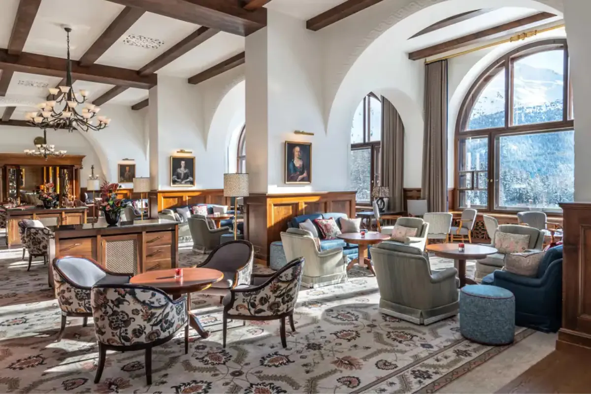 A tall-windowed lounge with double doors, upholstered furnishings, and alpine views