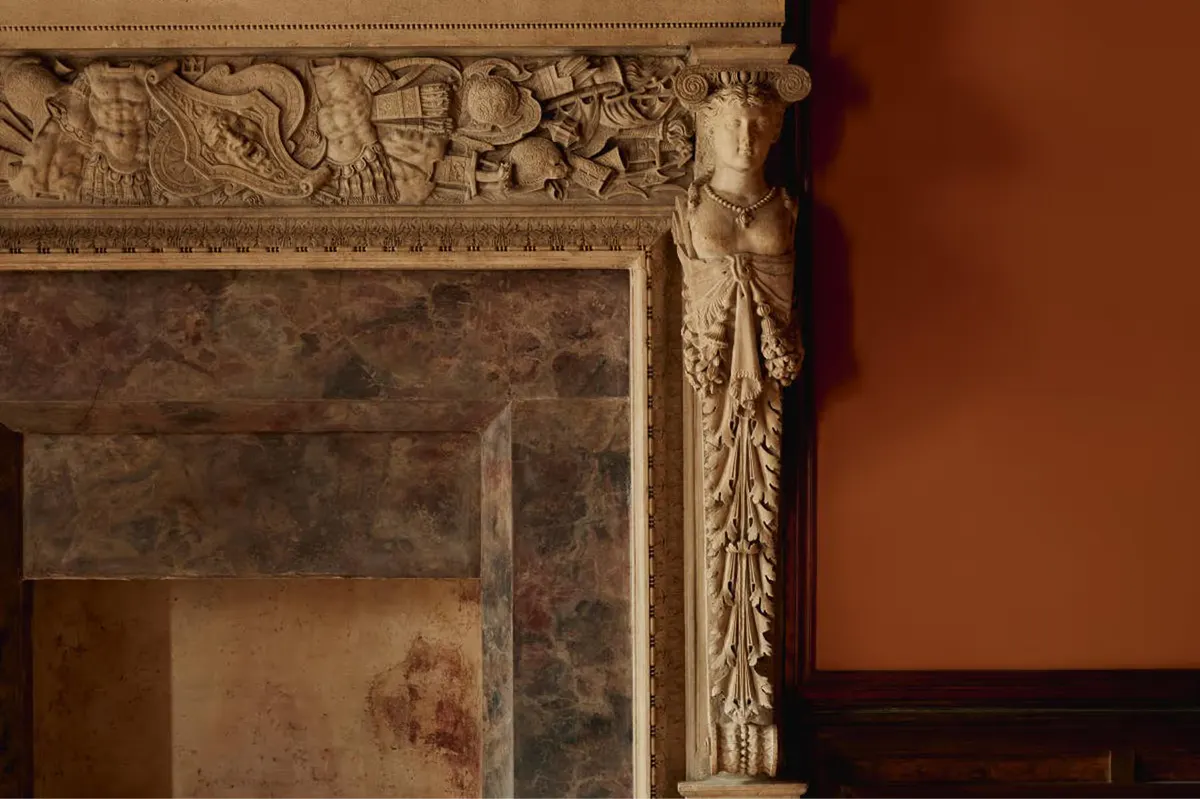 A close detail of an ornate fireplace mantel with carved stone decoration in cream and terracotta