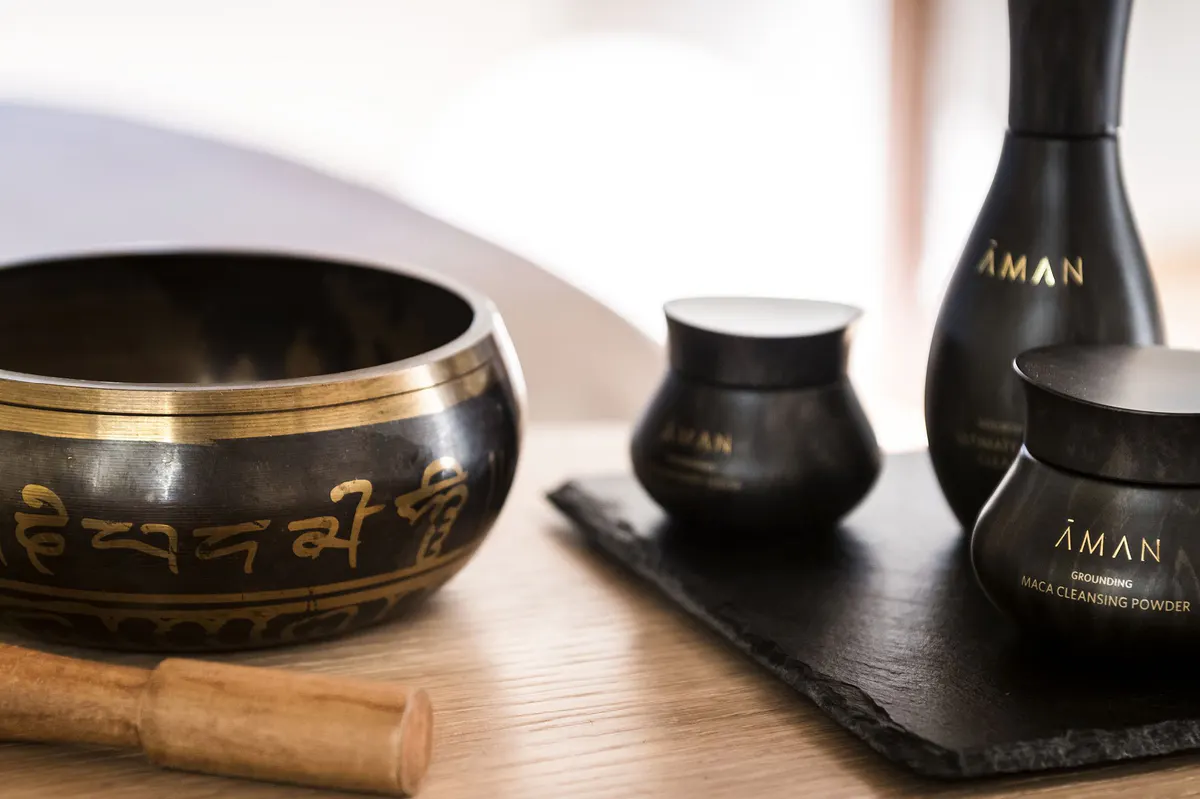 Aman wellness products including a black singing bowl, wooden mallet, and branded bottles