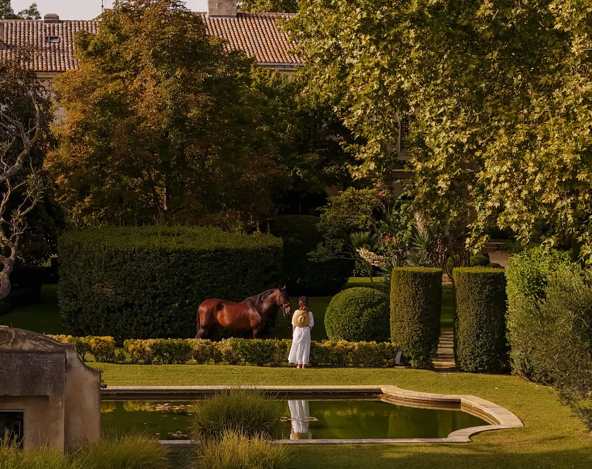 Equestrian guest on horseback in manicured garden with sculpted hedges and olive trees