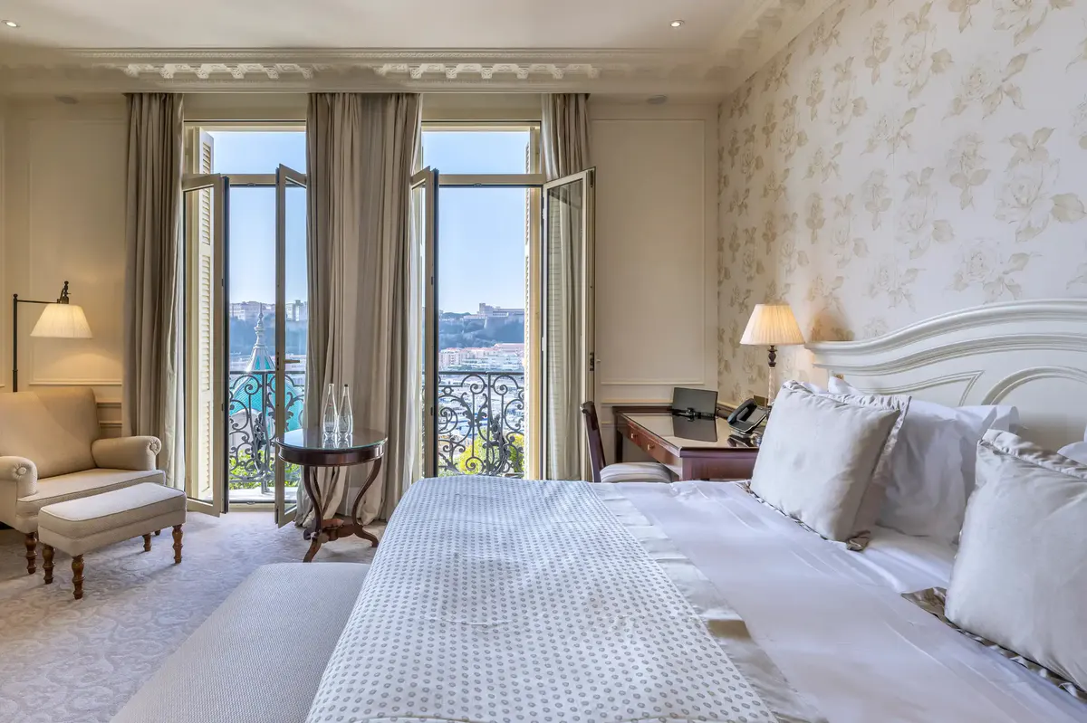 Suite bedroom with sea views through double doors, white bed and neutral furnishings