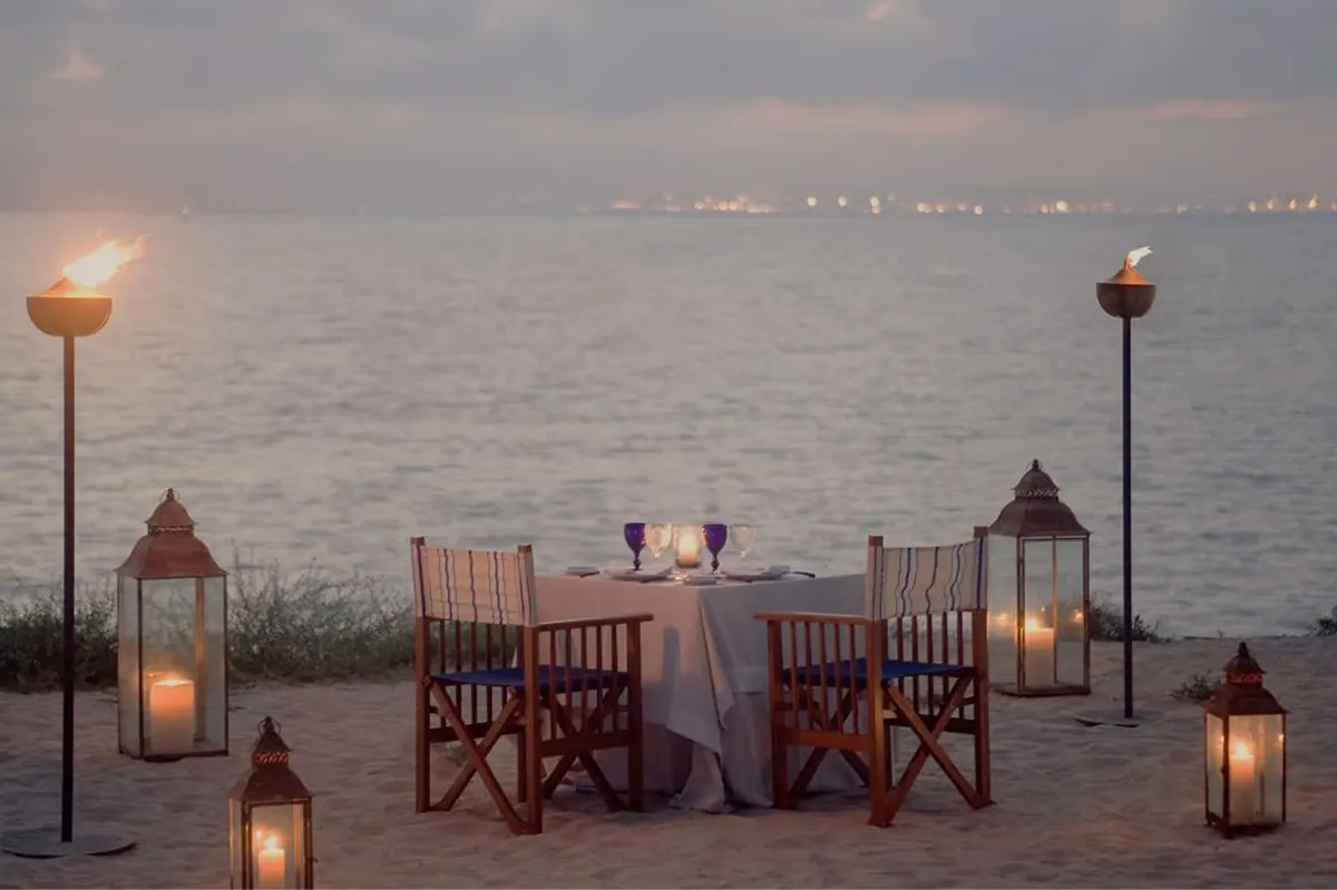 A terrace dining setting at twilight with wooden chairs, candlelit table, and bay views