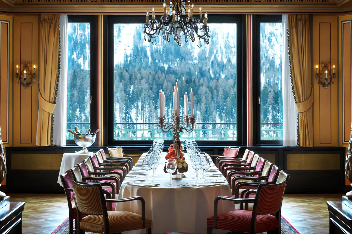 Long dining table with burgundy chairs, wood paneling, and alpine mountain views