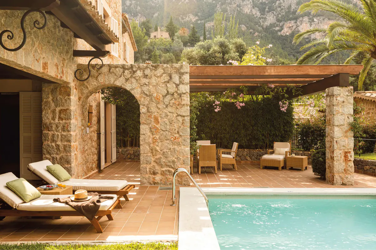 Stone villa with private pool, lounge seating, wooden pergola, and Mediterranean hillside setting