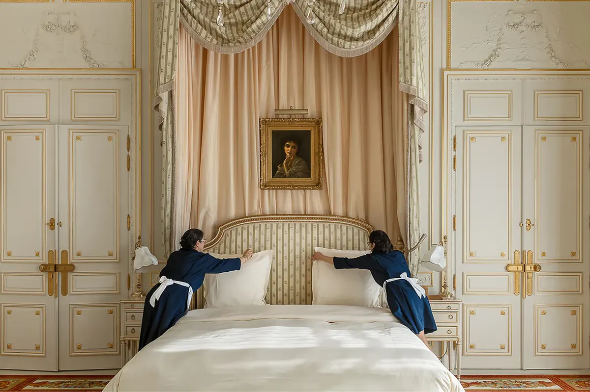 A bedroom with cream paneled doors, draped bed canopy, and classical gilt detailing